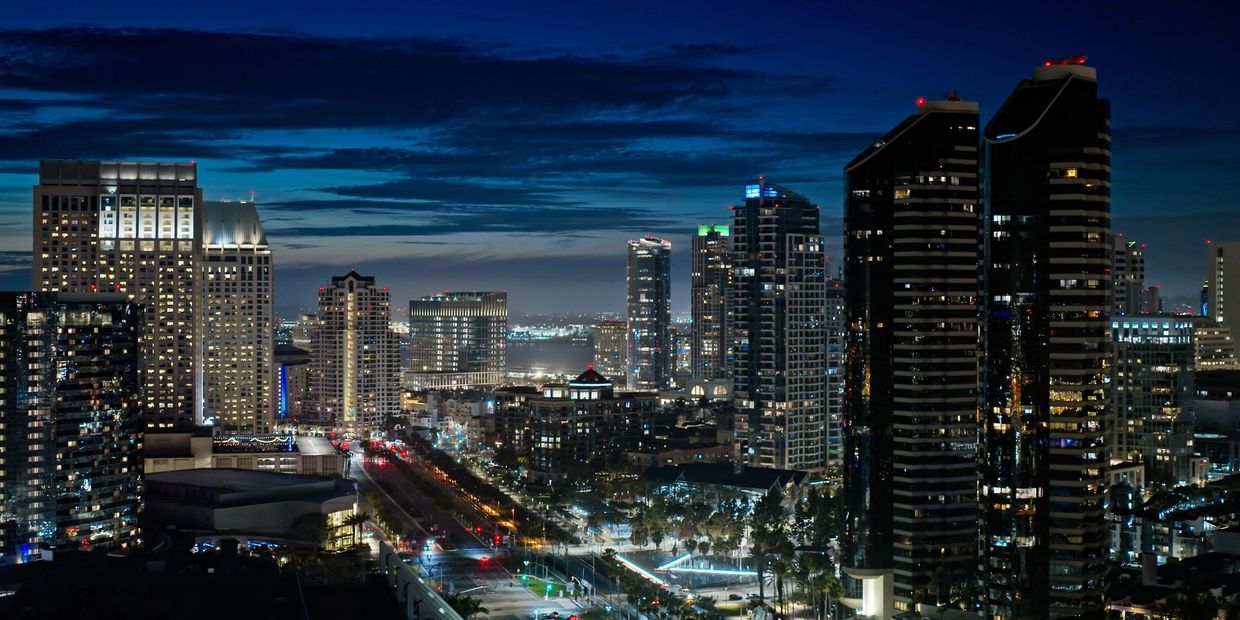 City skyline at night with illuminated skyscrapers and a dark blue sky.