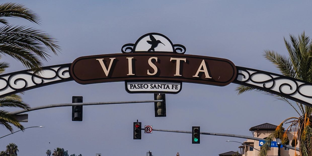 Entrance sign reading 'VISTA PASEO SANTA FE' with palm trees and traffic lights.