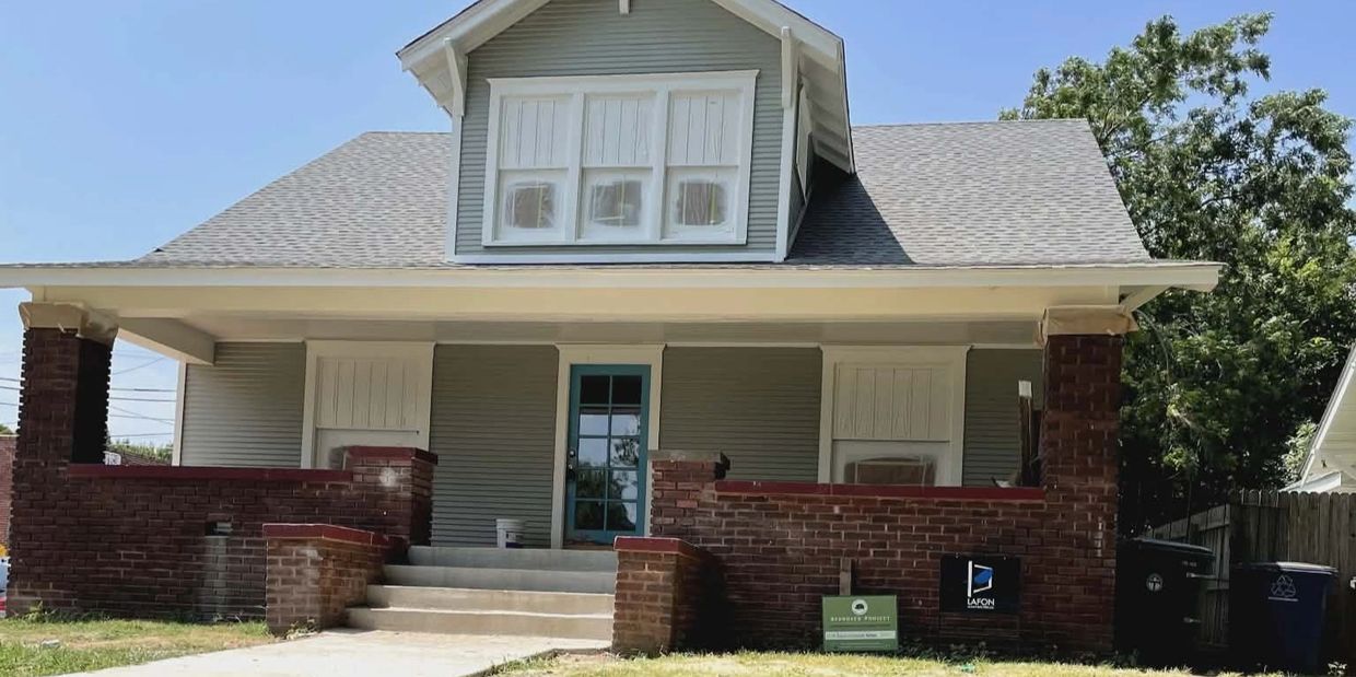 Classic house with brick porch and gray siding under a clear blue sky.