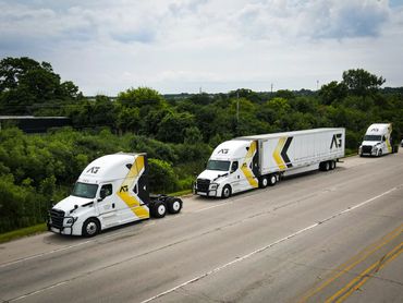 Three white trucks with yellow and black branding parked on a highway.