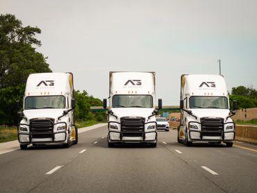 Three white semi trucks driving side by side on a highway.