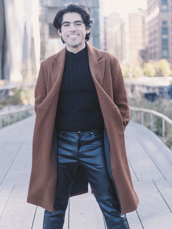 Smiling man in brown coat and black outfit on urban walkway.