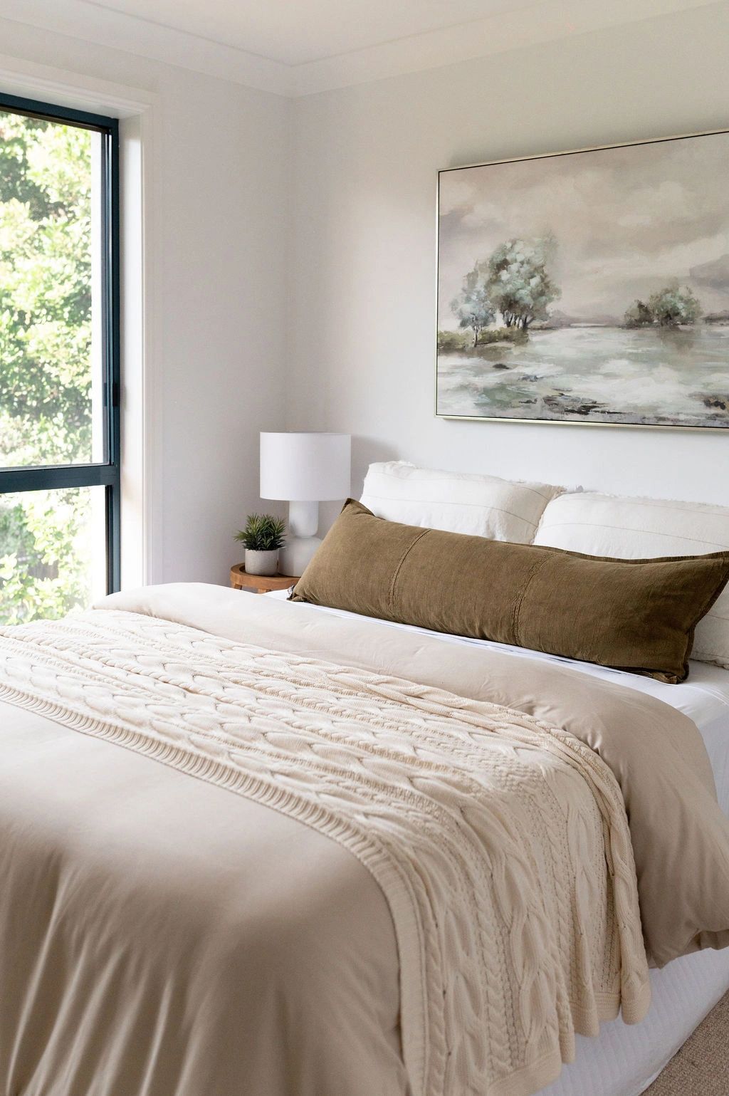 Cozy bedroom with neutral tones and a large green pillow.