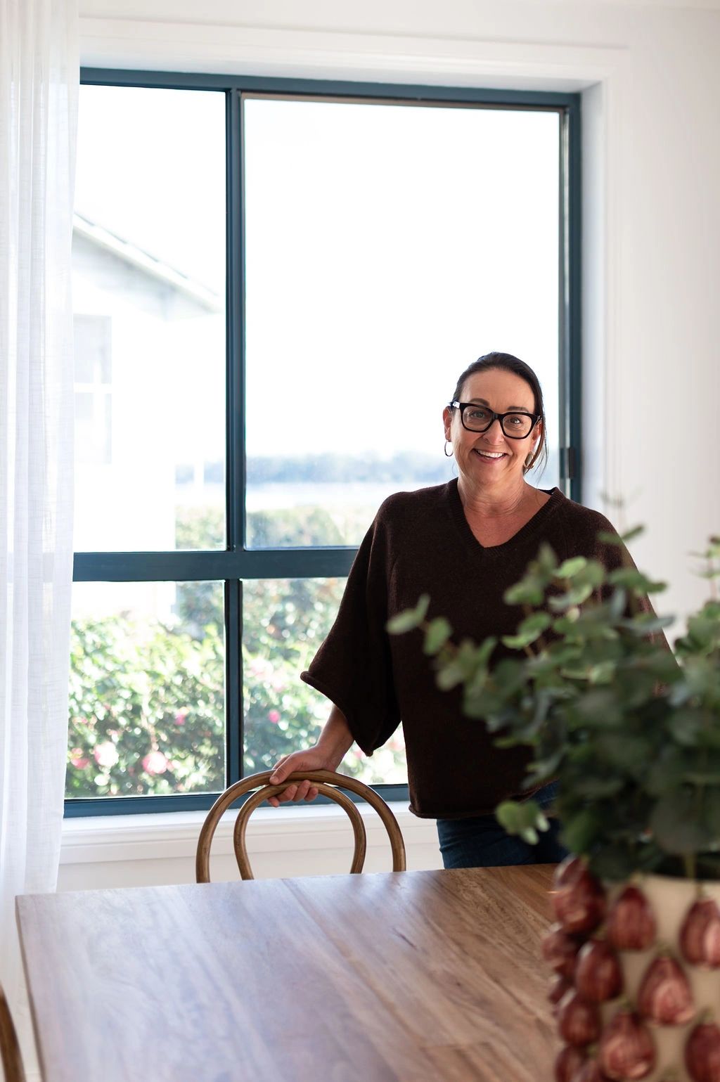 Smiling woman standing by a window in a cozy room.