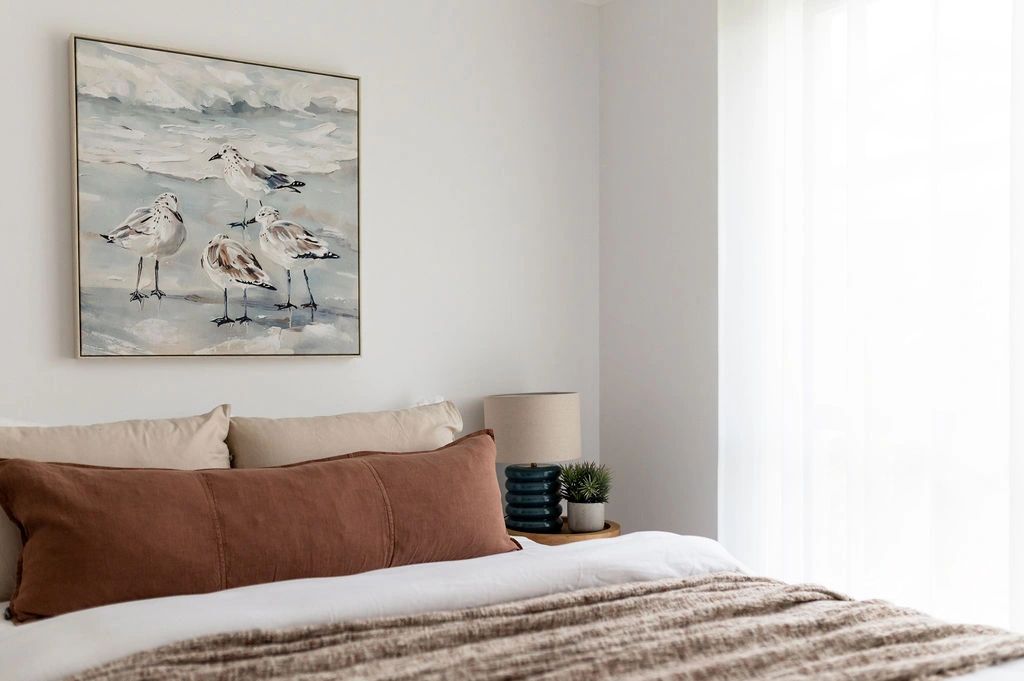 Cozy bedroom with bird painting and neutral tones.
