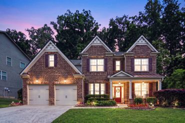 A brick two-story house with warm lights at dusk.