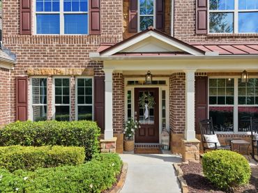 Brick house entrance with white pillars and manicured bushes.