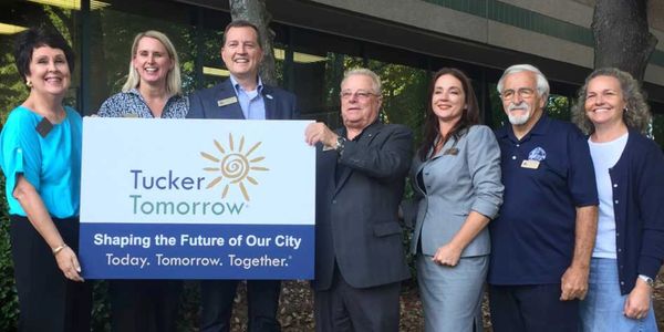 Seven people holding a sign for Tucker Tomorrow, promoting city development.