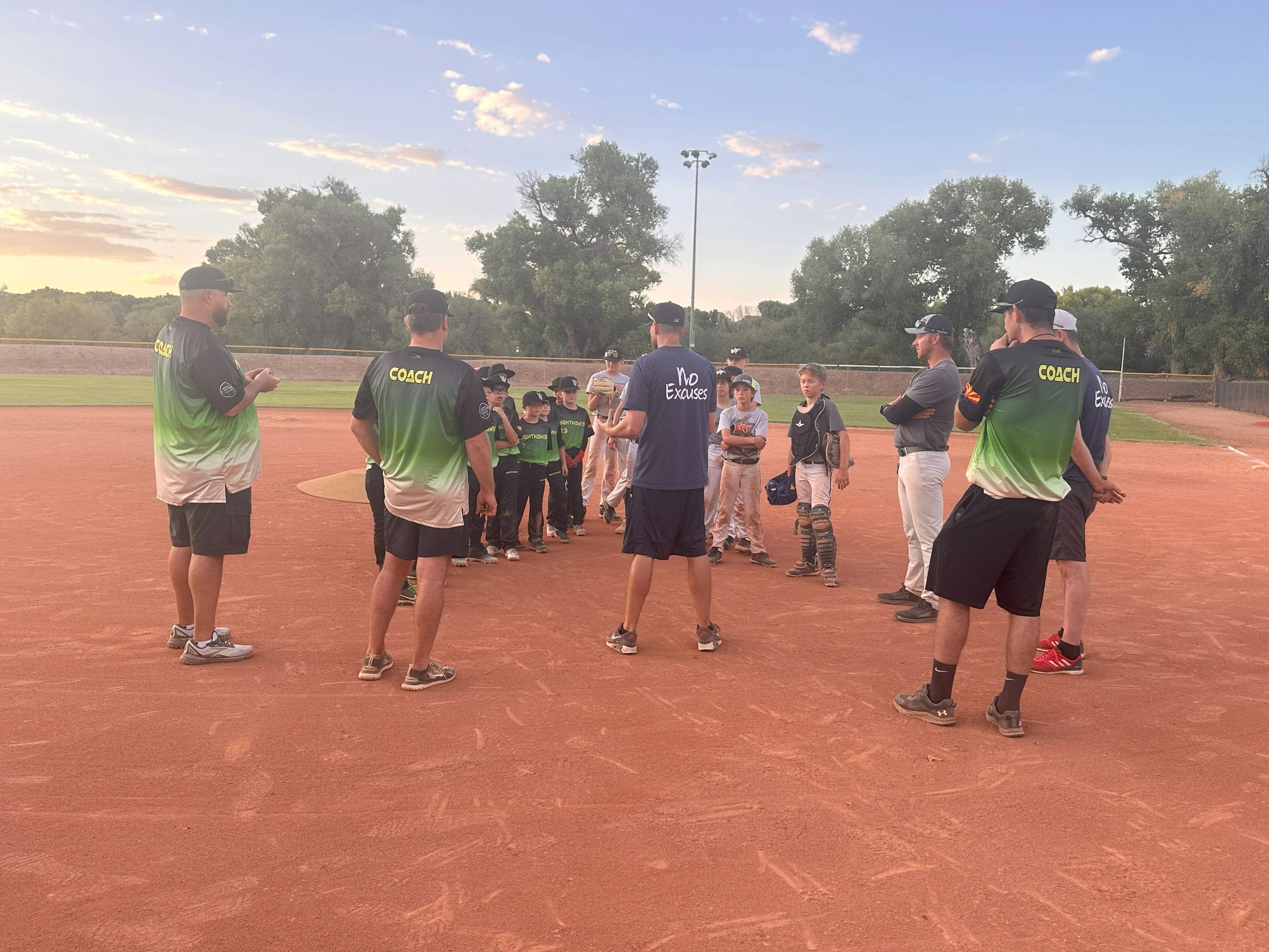 Coaches talk to kids at sunset on baseball diamond