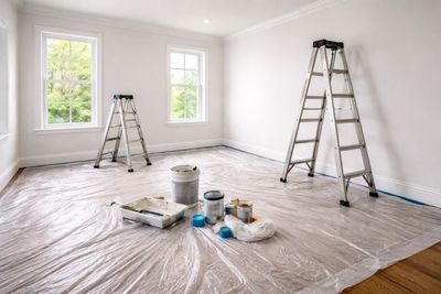 A room with plastic on the floors, ladders out and it is ready to be painted