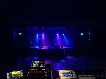 Dimly lit stage with purple lighting and audio equipment in the foreground.