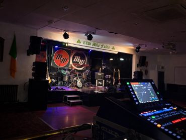 Dimly lit music stage with instruments and soundboard in foreground.