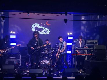 A band performs on stage under blue lights with a dragon and crescent moon projection.