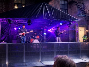A band performs live on an outdoor stage with purple lighting.