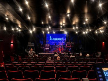 A dimly lit theater with a few people seated and a stage set for a performance.