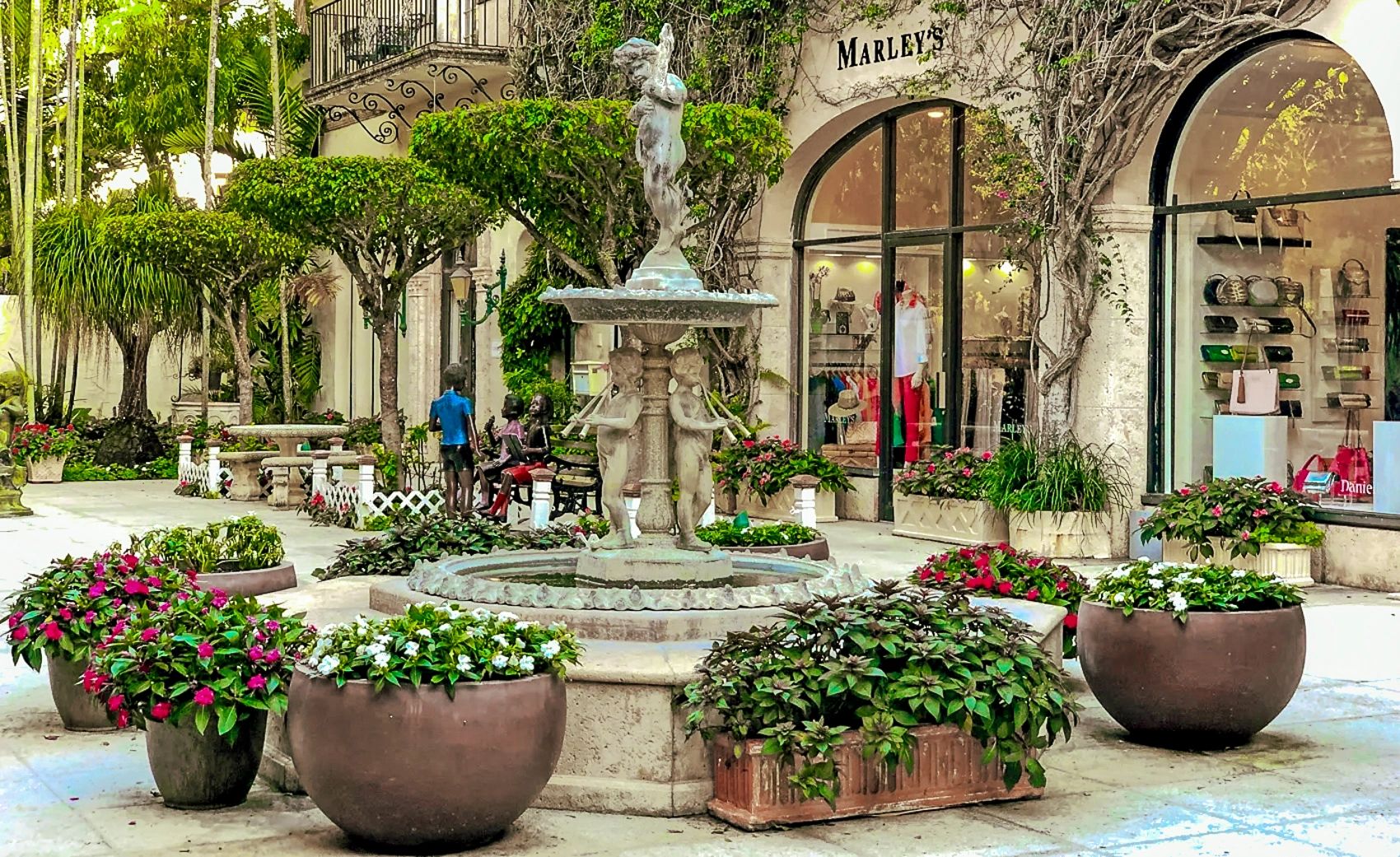 Charming courtyard with a central fountain and lush potted plants near a boutique named Marley’s Palm Beach Collection.