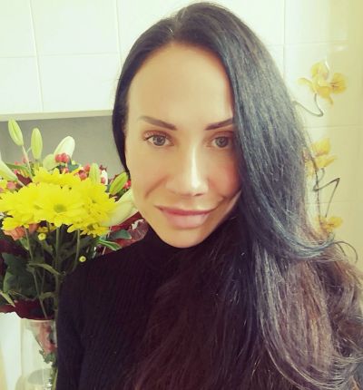Woman with long dark hair smiling near a bouquet of flowers.