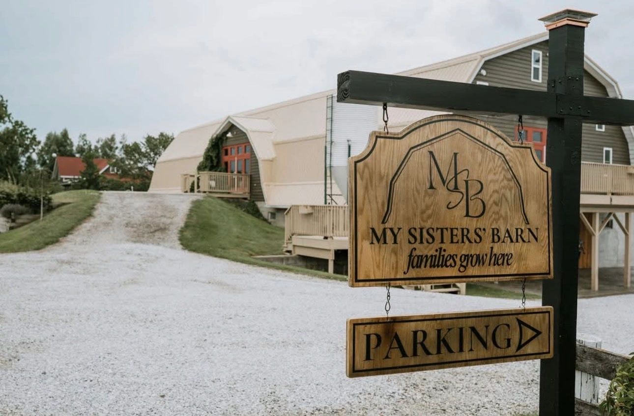 Wooden sign for My Sisters' Barn with parking directions in front of a large barn.