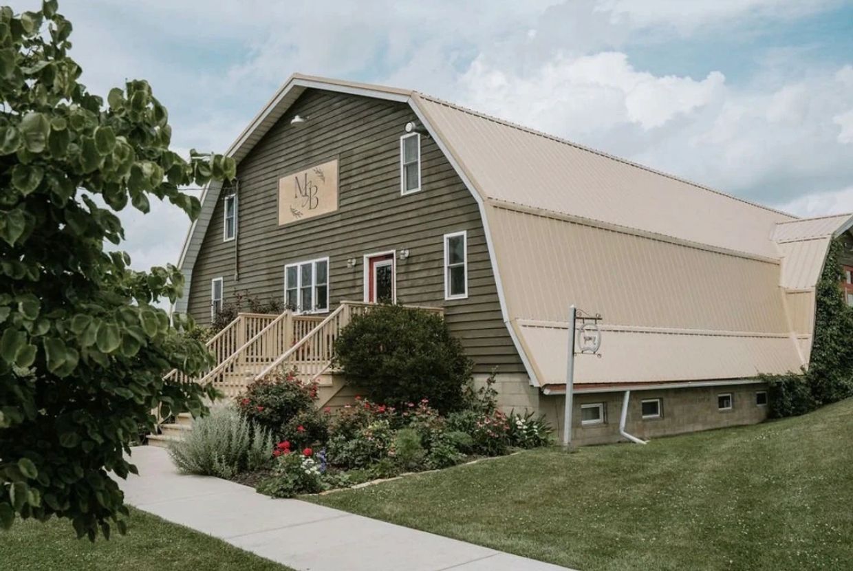 A rustic barn-style building with a garden and a sign labeled 'MB'.
