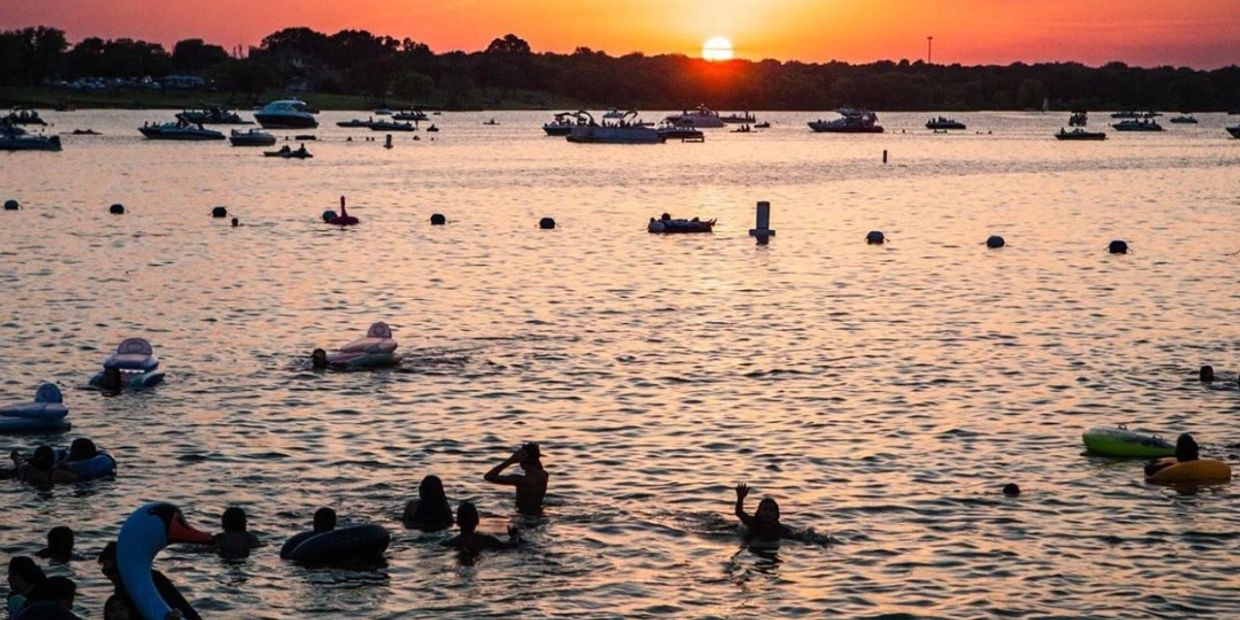 People swimming and boating on a lake during a colorful sunset.