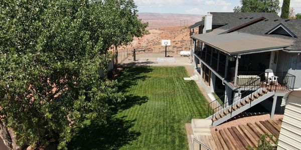 Backyard with green lawn, basketball hoop, and a covered porch on a sunny day.