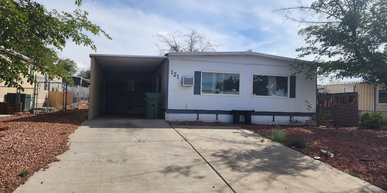 White mobile home with carport and dry landscaping under a blue sky.