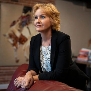 A thoughtful woman leans on a red couch, gazing ahead with a calm expression.Her name is Shanell Heely.