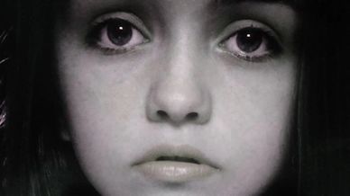 A ghostly image of a young girl's face peers out of darkness.