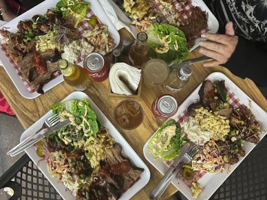Three plates of barbecue meals with drinks on a wooden table.