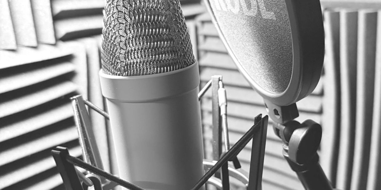 Close-up of a professional microphone with a pop filter in a soundproof studio.