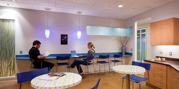Two people seated in a modern break room with blue chairs and tables.