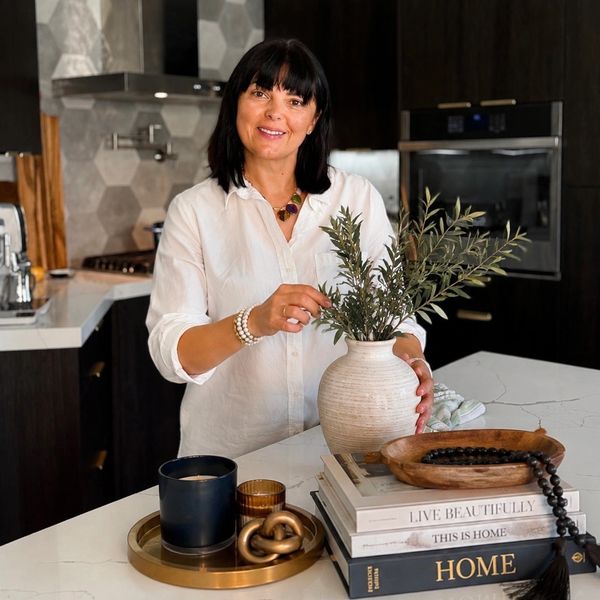 Woman arranging greenery in a vase on a kitchen island with decor.