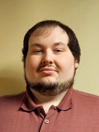 Man with short hair and beard wearing a maroon shirt.