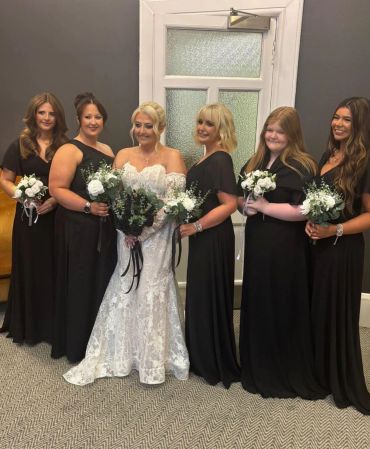 Bride with bridesmaids in black dresses holding bouquets.