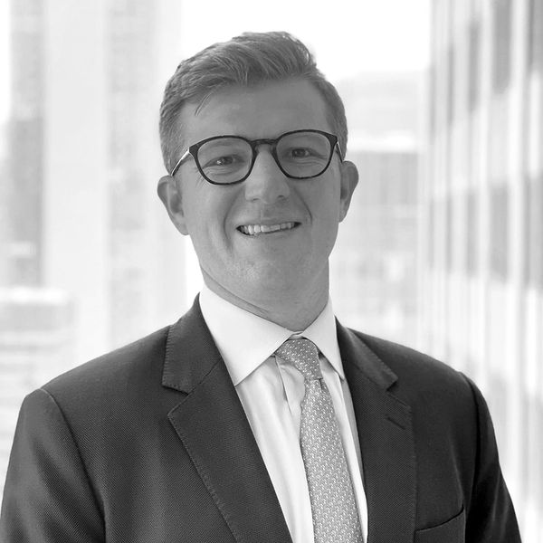 Smiling man in suit and glasses posing indoors with cityscape background.