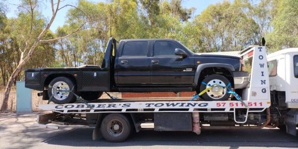 A large black American pickup truck on a flatbed tow truck being safely transported.