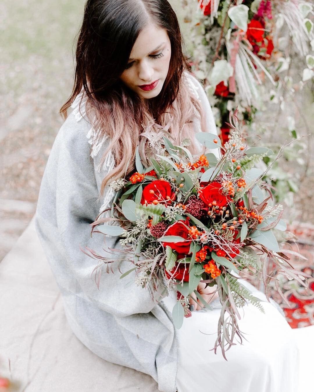 A woman in a gray shawl holding a vibrant bouquet of red flowers and greenery.