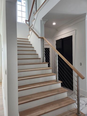 Modern wooden staircase with metal cable railing and natural light.