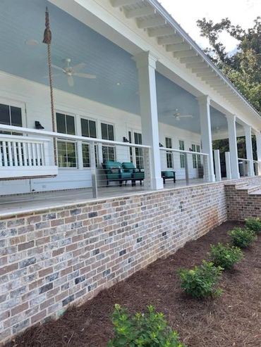 A spacious porch with white pillars, ceiling fans, and outdoor seating overlooking a garden.