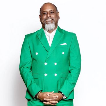 Man in a bright green suit smiling against a white background.