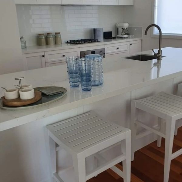 Modern white kitchen with island, blue glasses, and wooden stools.