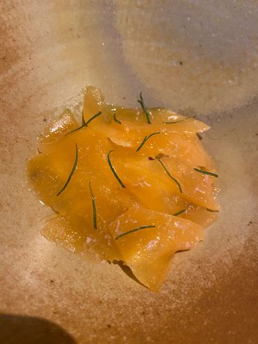 Thin orange slices with herbs on a rustic plate.