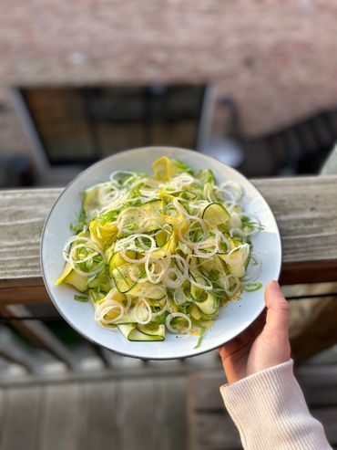 Fresh zucchini and yellow squash salad topped with thinly sliced onions and black pepper.