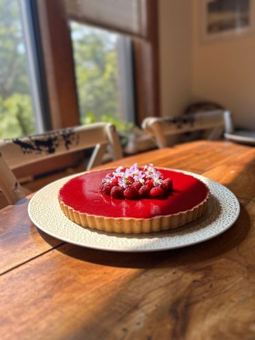A vibrant raspberry tart with fresh raspberries and small flowers on top.