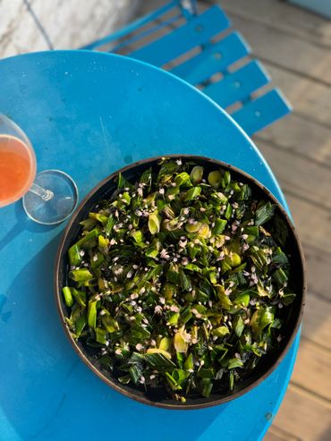 A bowl of chopped greens with edible flowers on a blue table.