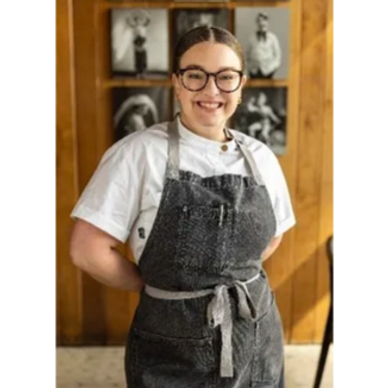 Smiling chef in glasses wearing a gray apron and white shirt.