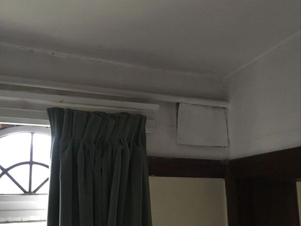 Green curtain hanging beside a small window with a vent above it.