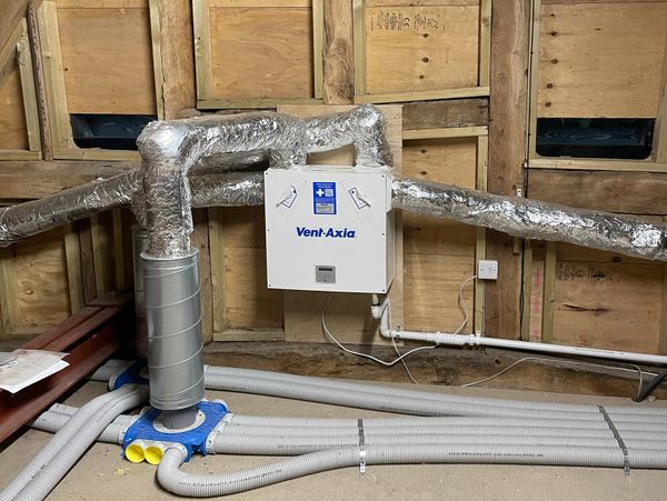 Ventilation system with insulated ducts and Vent-Axia unit installed in wooden-framed room.