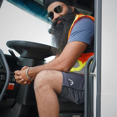 Bearded man with sunglasses and turban sitting in a vehicle wearing a safety vest.