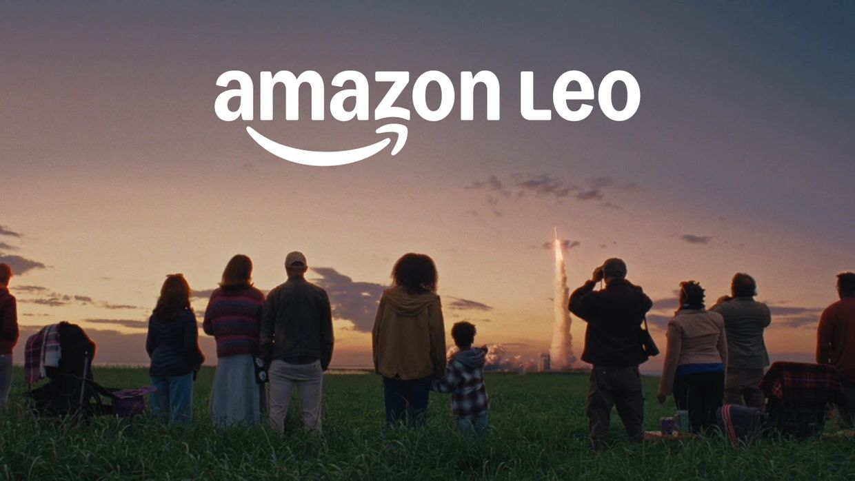 People watch a rocket launch at sunset with Amazon Leo branding above.